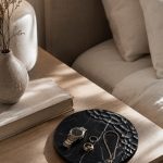 Chiseled black marble tray on a bedside table with a watch, gold rings and delicate chain jewelry