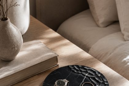 Chiseled black marble tray on a bedside table with a watch, gold rings and delicate chain jewelry