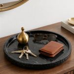 Black marble round tray with perfume, folded white towel and gold bracelets on a marble counter