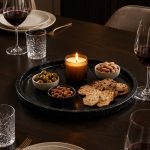 Black marble round tray styled with olive bowls, almonds, crackers and a candle for charcuterie