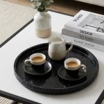 Round black marble tray with espresso cups and ceramic jug on a coffee table
