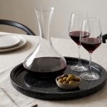Round black marble tray with pillar candle, book and espresso cup on a wooden coffee table