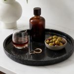 Black marble catchall tray with brass ornament, sunglasses, wallet and keys on a wooden entryway dresser