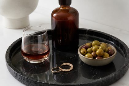 Black marble catchall tray with brass ornament, sunglasses, wallet and keys on a wooden entryway dresser