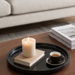 Black marble tray with two espresso cups and a lit pillar candle on a walnut coffee table
